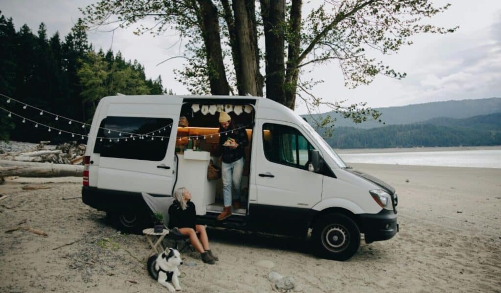 A man, woman and a dog sitting next to a white camper van.