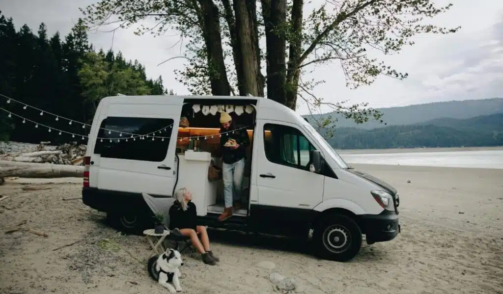 A man, woman and a dog sitting next to a white camper van.